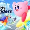 Una scena di gameplay frenetica di Kirby Air Riders, che mostra Kirby e altri personaggi su vari veicoli che usano le loro abilità in una pista colorata, con il logo di Nintendo Switch 2.